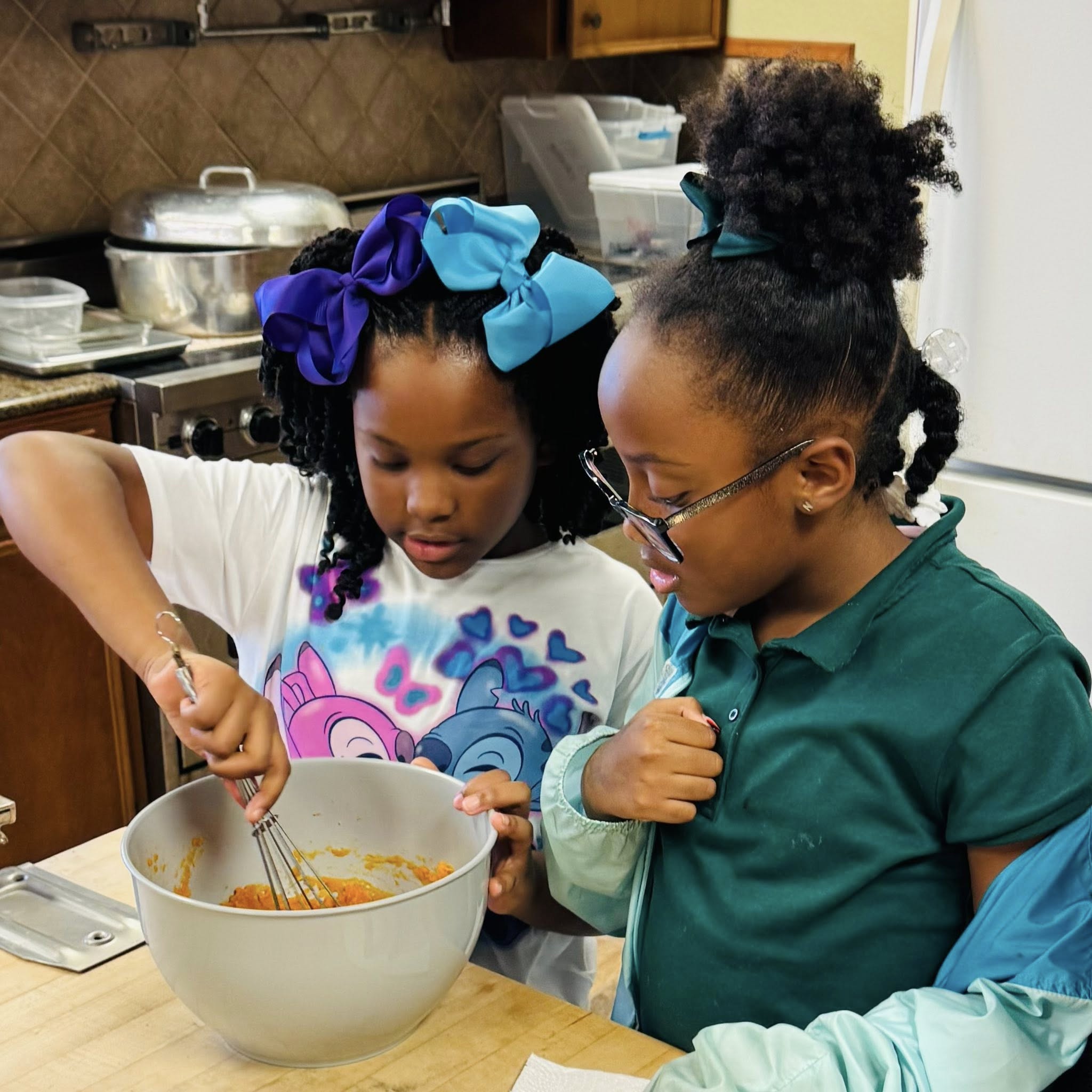 One girl watching another girl whisk something in a bowl.